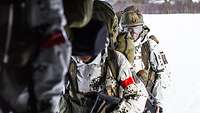 Three mountain infantry soldiers march in single file carrying their heavy backpacks.