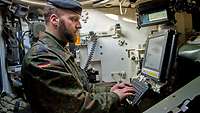 A crew member sitting at a computer screen inside a main battle tank types on a keyboard.