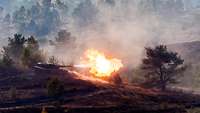 A Leopard 2 MBT fires on open ground.