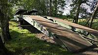 Ein Brückenlegepanzer fährt seine Brücke über einen breiten Graben in einem Wald aus.