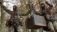 Two soldiers move hand over hand along a double rope walk above rough terrain as part of their aptitude assessment 