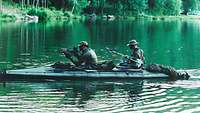 Two soldiers cross a river in a canoe; the man in front holds his weapon at the ready.