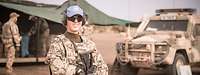 Soldatin steht mit Ausrüstung vor einem Fahrzeug