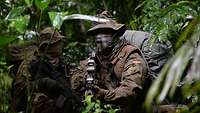 Two soldiers move through a rain forest with weapons at the ready.