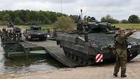 Ein Panzer der Bundeswehr fährt von einer Schwimmschnellbrücke ans Ufer, ein zweiter folgt ihm.