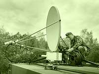 The signal corps establishes and maintains communications. A soldier setting up a satellite antenna on a rooftop.
