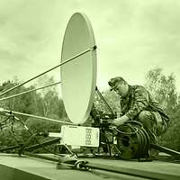 A soldier setting up a satellite antenna on a rooftop.