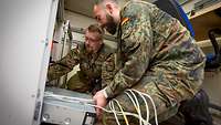 Two soldiers kneeling to fit a computer into a server cabinet.
