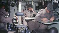 Drei Soldaten sitzen im Inneren eines Panzers. Sie notieren Meldungen und geben Funksprüche weiter.