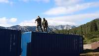 Zwei Soldaten befestigen die Transportgurte auf der Oberseite eines Containers. 