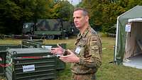 Oberstleutnant Steinhagen steht vor einem Zelt und spricht.