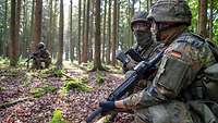 Drei Soldaten knien mit ihrem Gewehr in einem Waldstück und sondieren die Lage.