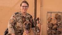 Eine Soldatin kniet mit einem Spürhund vor sich auf dem Boden