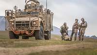 Drei lettische Soldaten stehen neben einem gepanzerten Fahrezug