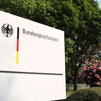 Ein Schild mit der Aufschrift Bundessprachenamt vor Bäumen und Himmel.