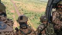 Mehrere Soldaten sitzen bei offener Tür im fliegenden Helikopter