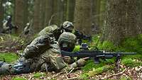 Zwei Soldaten gehen in einem Waldstück mit Waffe in Deckung.