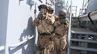 Drei Soldaten laufen eine Treppe am Oberdeck herunter und sichern dabei ihre Umgebung