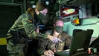 In einem Wartungscontainer stehen zwei Soldaten vor einem Laptop.