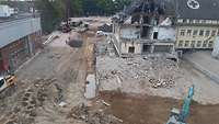 Blick aus der Höhe auf eine Baustelle, auf der rechts unter anderem ein altes Gebäude abgebrochen wird