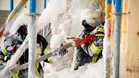 Zwei Feuerwehrleute voll Schaum vor einem Testraum