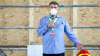 Dipl. Wirt. Ing. (FH) Günter Knopf Ein Mann in Freizeitkleidung mit einer FFP 2 Maske und einem Mikrofonin der Hand