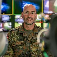 Ein Soldat steht zwischen Fernsehkameras vor zahlreichen Monitoren