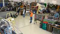 Two fixed wing aircraft and a helicopter in a hangar. A man explaining something to five young men