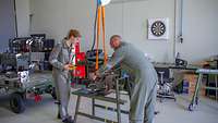 Positionierung der Bordkanone Zwei Waffenmechaniker bewegen mithilfe eines Deckenkrans die Bordkanone in der Werkstatt