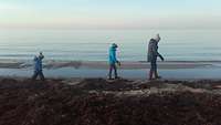 Eine Frau und zwei Kinder laufen am Strand.