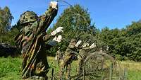 Eine Gruppe von Soldaten legt auf einer Wiese Stacheldrahtschlingen auf ein Metallgestell.