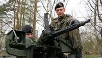 Zwei Soldaten stehen hinter einem Maschinengewehr, das auf einem Spähwagen Fennek montiert ist.