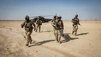 Fünf Soldaten, zwei davon mit einer Trage in der Hand, entfernen sich rasch von einem Hubschrauber