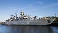 Ein graues Kriegsschiff liegt in einem Hafen.
