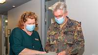 Eine Mitarbeiterin des Gesundheitsamtes Köln mit einer Liste in der Hand neben einem Soldaten. 