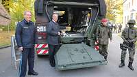 Je ein Vertreter der Polizei, der Bundeswehr und der Politik stehen an einem GTK Boxer.