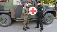 Ein Soldat und ein Polizeibeamter unterhalten sich vor einem Fahrzeug des Sanitätslehrregiments.
