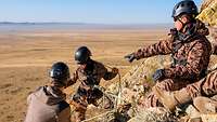 Drei Soldaten stehen mit Kletterausrüstung an einem Berg.