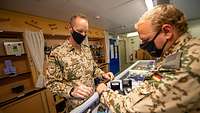 Zwei Soldaten mit Mund- Nasen-Bedeckung stehen an einem Tresen und betrachten verschiedene Uhren