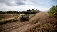 Ein Kampfpanzer vom Typ Leopard 2 fährt durch sandiges Gelände