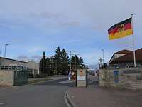 Kasernentor, seitlich mit niedrigen Mauern und einer Deutschlandflagge mit Adler