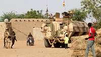 Ein gepanzertes Fahrzeug fährt durch eine afrikanische Siedlung. Einheimische schauen ihm nach.