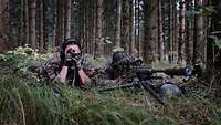 Zwei Soldaten liegen getarnt im Gras und beobachten das vor ihnen liegende Gelände durch ein Fernglas.