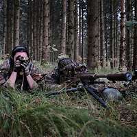 Zwei Soldaten liegen getarnt im Gras und beobachten das vor ihnen liegende Gelände durch ein Fernglas.