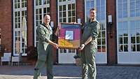 Der Inspekteur der Luftwaffe und der Kommodore des LTG 62 halten gemeinsam einen Rahmen mit einer Deutschen Flagge darin.