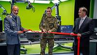 Handover of the virtual studio at the Operational Communication Center Two soldiers and a man in a suit stand outside the studio, jointly holding a red ribbon in their hands