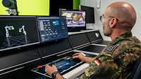 A soldier sits in front of several screens and operates a keyboard with both hands