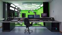 Technical control elements and computers are located in one room. Behind them, camera robots stand in front of a green wall
