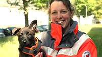 Christina Sonntag in her DRK personal protective equipment, holding puppy Aruba