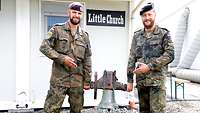 Pastoralreferent Diewald und sein Unterstützungsfeldwebel stehen mit der Glocke vor der Kirche